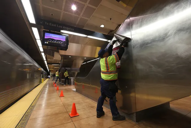 Transit workers installing warning signs on metal wall at Los Angeles metro station