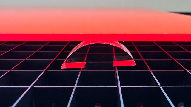 Pièce en acrylique découpée avec la machine de découpe laser Trotec montrant un bord courbe propre sur un lit laser en nid d'abeille.