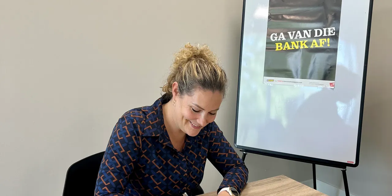 Vrouw ondertekent document aan tafel met IK BINDR-promotieposter op achtergrond