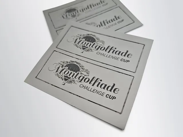 Étiquettes métalliques marquées au laser avec le motif de la Montgolfiade Challenge Cup, réalisées à l'aide d'une machine de marquage laser Trotec.