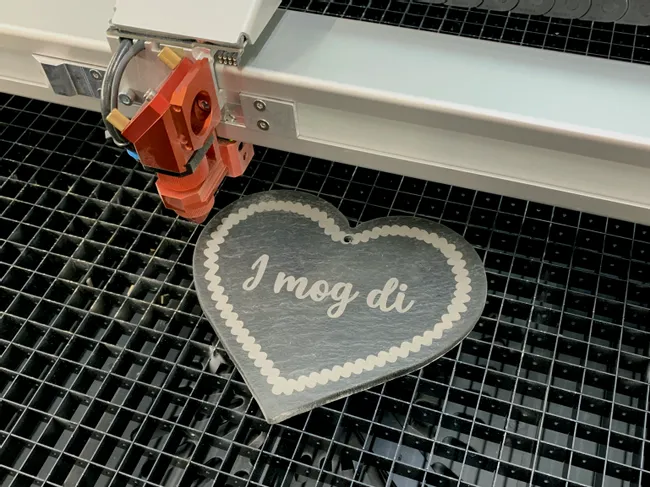 Trotec laser cutter engraving heart-shaped slate sign with 'I mog di' text