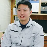 木製の棚とカレンダーを背景にオフィスに座る作業着姿の男性
