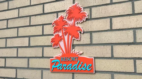 Trotec laser-cut acrylic sign with palm trees and Resort Paradise text mounted on brick wall