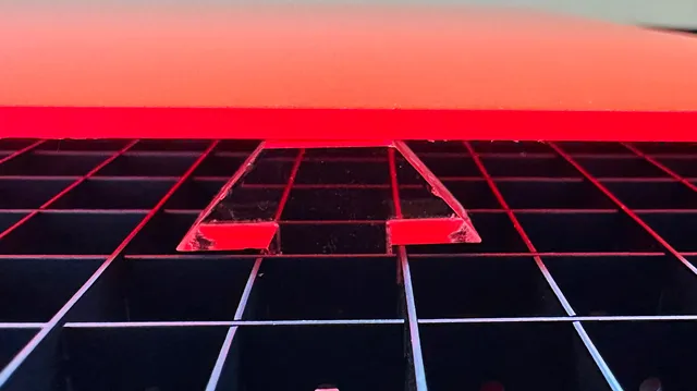 Plaque acrylique rouge découpée au laser sur le plateau de découpe nid d'abeilles de Trotec.