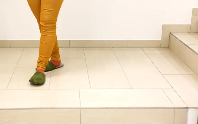 Orang bercelana kuning dan sandal hijau berjalan di dekat tangga keramik