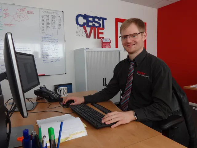 Werknemer van Trotec aan bureau in kantoor met lasergravure evenementschema op whiteboard