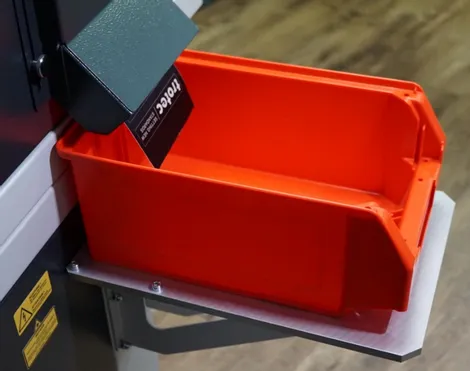 System do znakowania laserowego Trotec zrzuca grawerowaną metalową przywieszkę do czerwonego pojemnika na części.