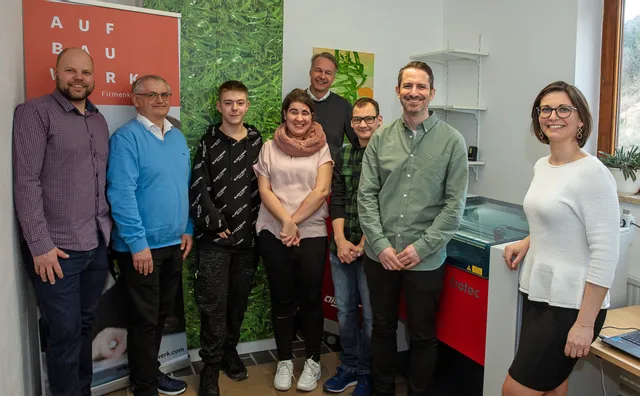 Group standing beside Trotec Speedy series laser cutter in workshop setting