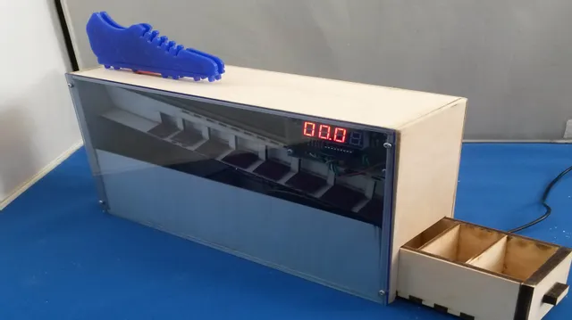 Boîtier électronique en bois découpé au laser avec écran LED et chaussure bleue imprimée en 3D sur le dessus.