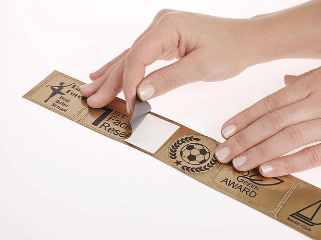 Hands peeling masking tape from laser-engraved acrylic awards made with Trotec laser cutter