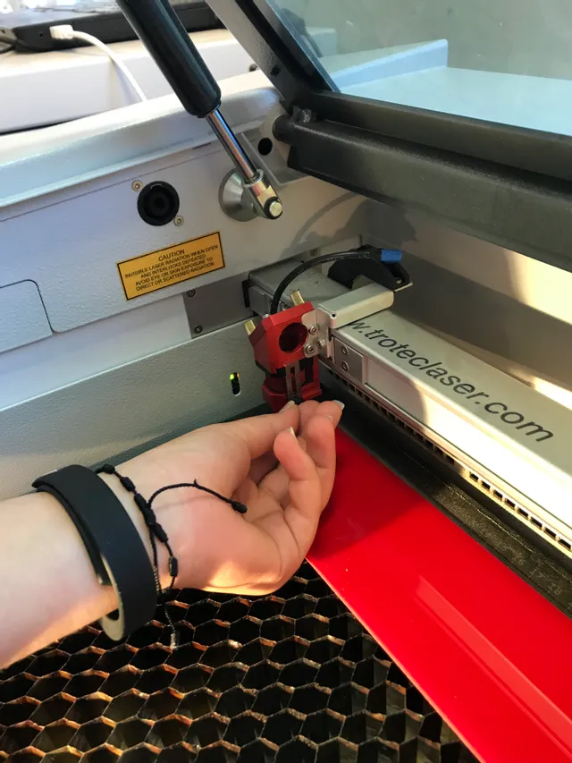 Hand adjusting focus tool on Trotec Speedy series CO₂ laser cutter inside engraving area
