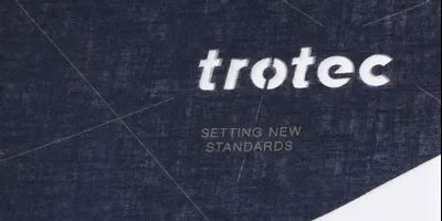 Trotec lasergeschnittenes Textil mit präziser Gravur des Logos und dem Slogan 'Setting New Standards'.