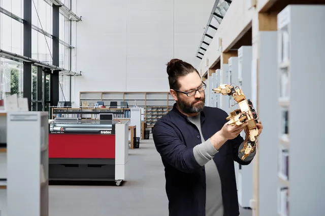 L'uomo esamina il prototipo di braccio robotico vicino alla taglierina laser Trotec Speedy 400 flexx CO₂ in uno spazio di lavoro moderno