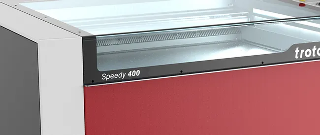Mesin ukiran laser Trotec Speedy 400 CO₂ dengan tutup transparan pada roda kastor
