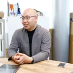 近代的なワークスペースのデスクに座り、タブレットを使ってレーザー彫刻機について話す男性。