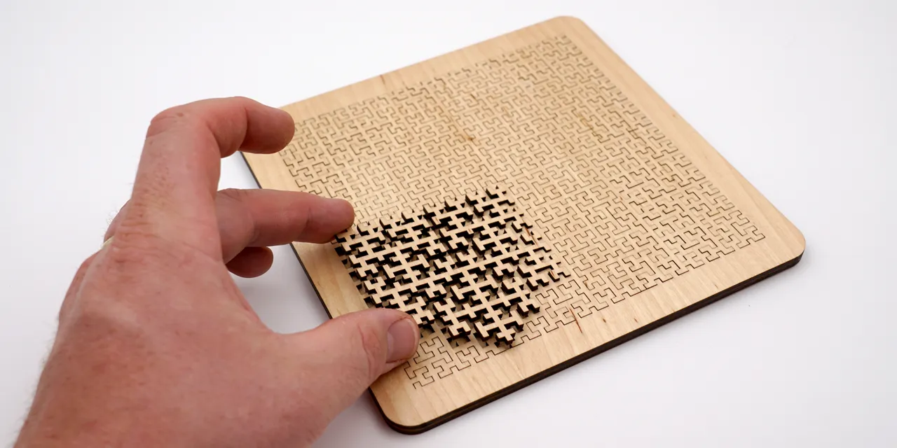Hand removing piece from intricate wooden puzzle cut with Trotec CO₂ laser cutter