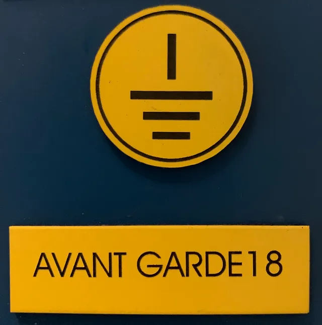 Laser-engraved yellow sign with grounding symbol and text Avant Garde18, likely made with Trotec laser cutter