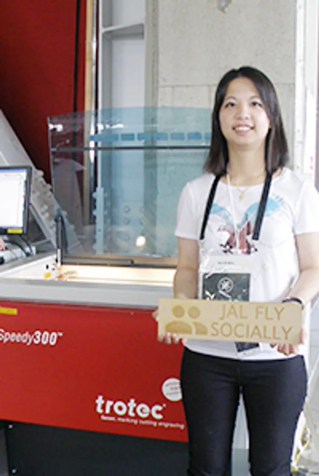 トロテック・レーザーカッターSpeedy 300 CO₂のそばで彫刻された木製看板を持つ女性。