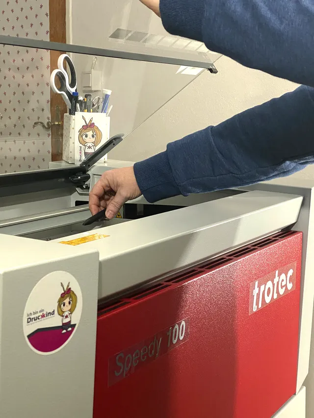 User adjusting material inside Trotec Speedy 100 CO₂ laser engraving machine