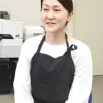 オフィスでレーザープリンターの近くに座る黒いエプロン姿の女性（トロテック・レーザー機器は見えません