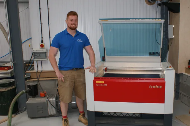 Hombre de pie junto a una cortadora láser Trotec Speedy 400 CO₂ en un taller industrial