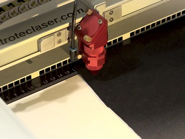 Trotec Laserschneider Kopf graviert schwarzes Material auf Arbeitstisch mit Lineal Skala