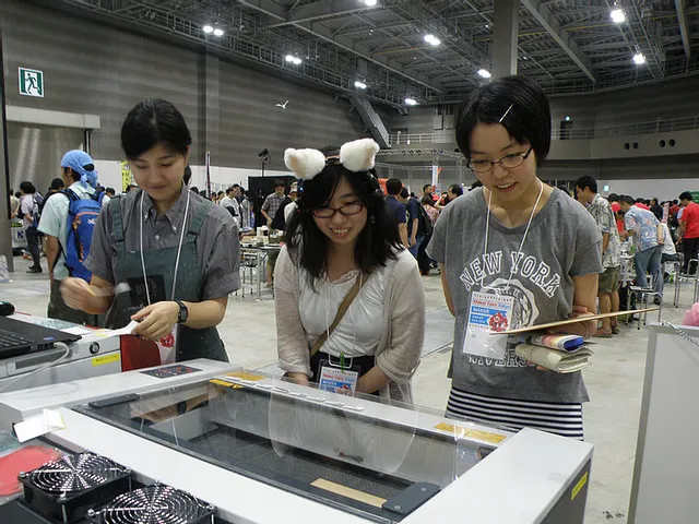 メーカーフェアのブースでレーザーカッターによる木材彫刻に見入る来場者たち