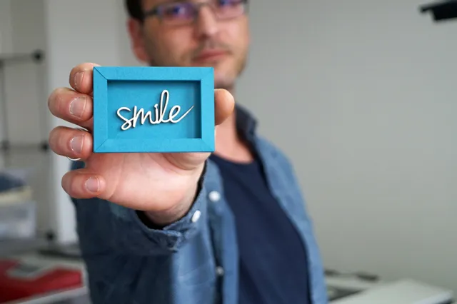 Person holding laser-cut smile sign made with Trotec laser cutter in blue paper frame