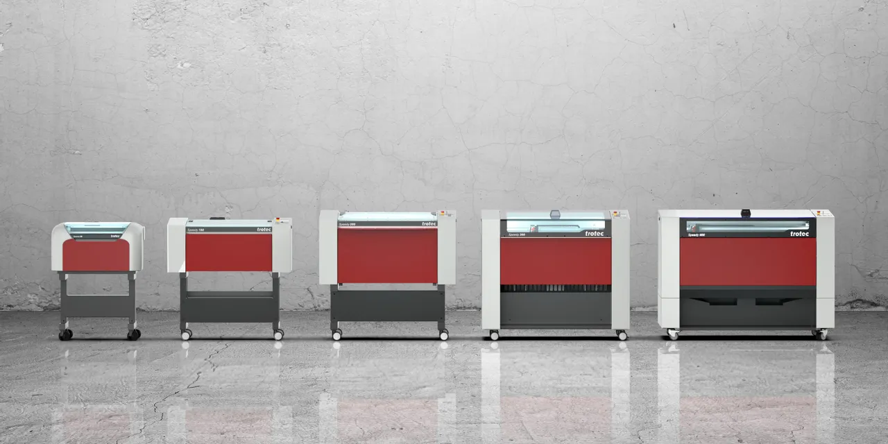 Lineup of Trotec Speedy series CO₂ laser cutters and engravers against concrete wall background