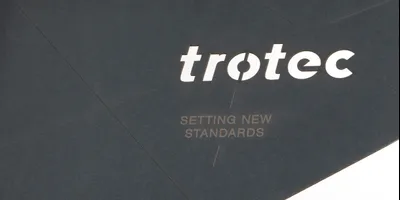 Trotec Laser-geschnittener und gravierter schwarzer Karton mit Logo und dem Slogan 'Setting New Standards'.