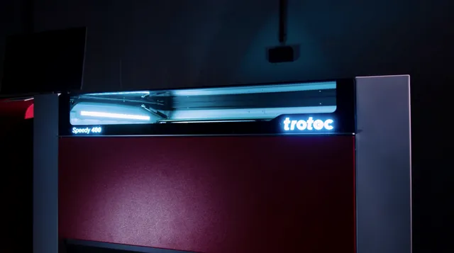 Máquina de corte a laser Trotec Speedy 400 CO₂ iluminada em um espaço de trabalho escuro