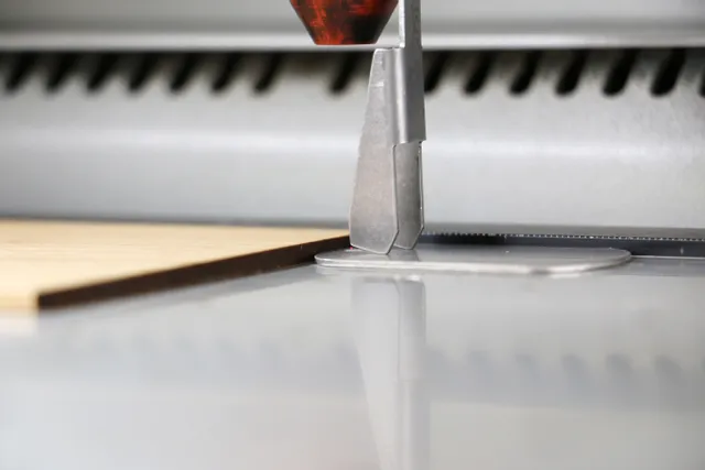 Gros plan de la buse de la machine de découpe laser Trotec se focalisant sur une feuille de bois pour une gravure précise.