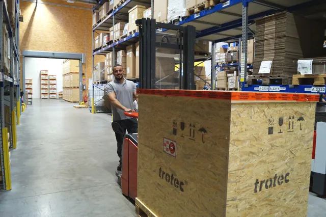Caja de la cortadora láser Trotec siendo transportada en el almacén por un empleado con transpaleta