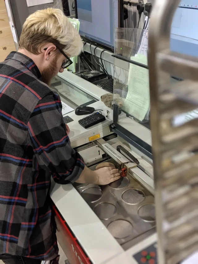 Bediener positioniert Material in den Laserschneidern der Speedy-Serie von Trotec für die Einrichtung der Gravur