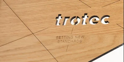 Panneau en bois découpé et gravé au laser par Trotec, affichant le logo et le slogan de la marque.