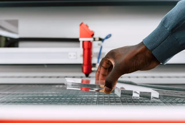 Handmatige plaatsing van een heldere acrylplaat op een bed van een CO₂-lasersnijder uit de Trotec Speedy-serie
