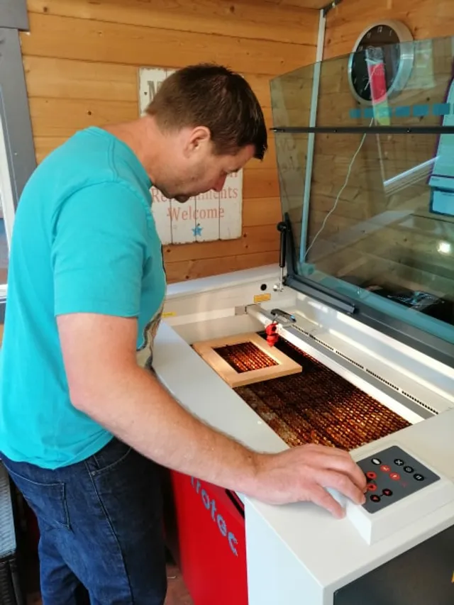 Man operating Trotec Speedy series CO₂ laser cutter engraving wood in workshop