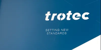 Trotec-Logo mit Slogan 'Setting new standards' auf blauem Hintergrund