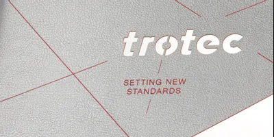Trotec lasergeschnittenes Logo und Slogan auf strukturiertem grauem Material mit CO₂ Lasergravierer-Technologie