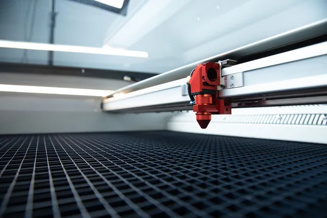 Vista de perto do cabeçote da máquina de corte a laser de CO₂ da linha Trotec Speedy sobre a mesa de gravação