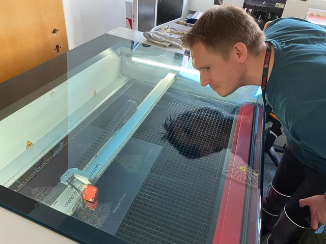 Man observing Trotec Speedy series CO₂ laser cutter engraving acrylic sheet