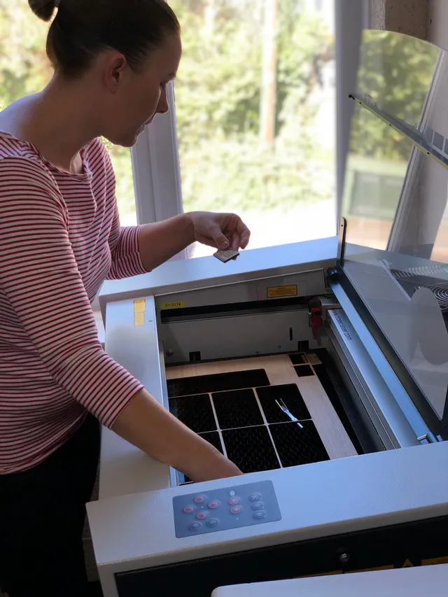 Frau mit Trotec Laserschneider, um ein graviertes Holzstück von einem Lasersystem der Speedy-Serie CO₂ zu entfernen