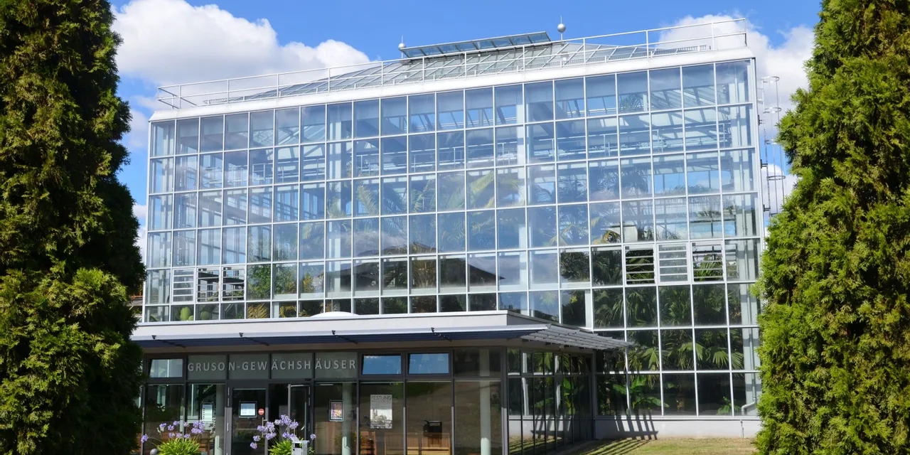 Glass exterior of Gruson-Gewächshäuser greenhouse with tropical plants and blue sky reflected