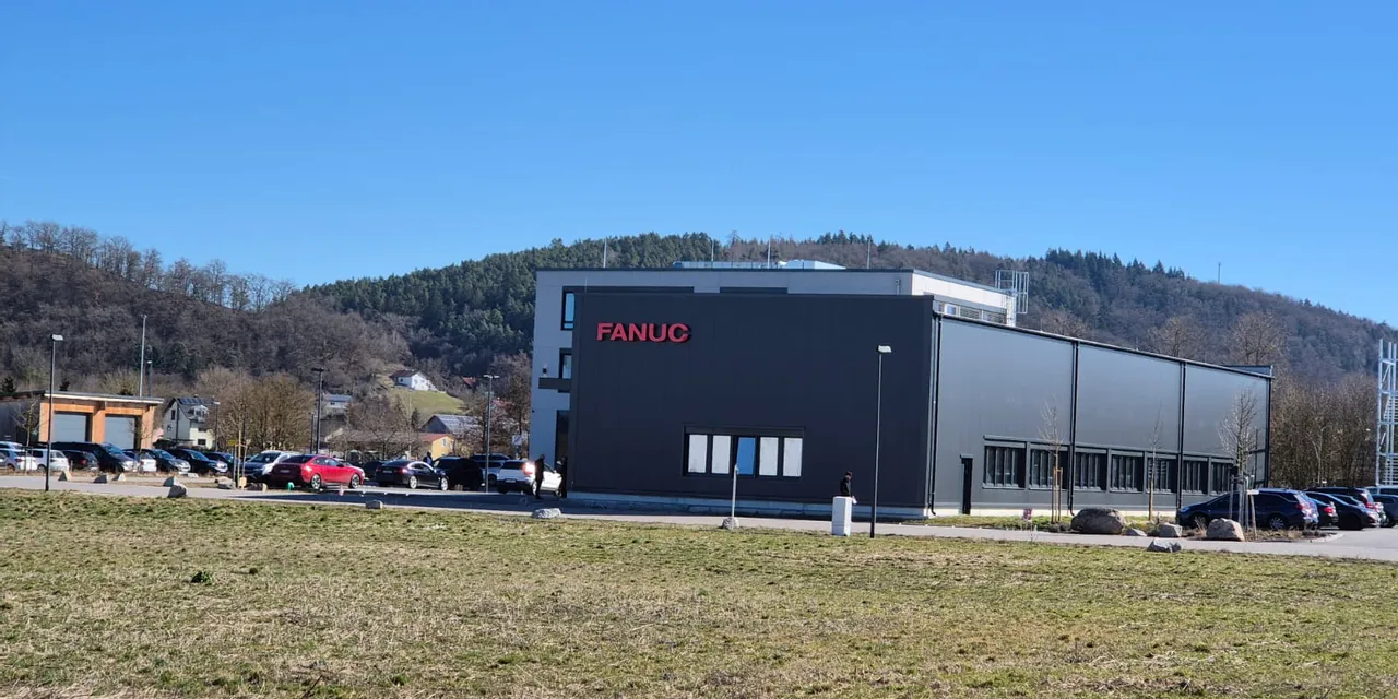 FANUC Industriegebäude mit geparkten Autos und bewaldeten Hügeln im Hintergrund