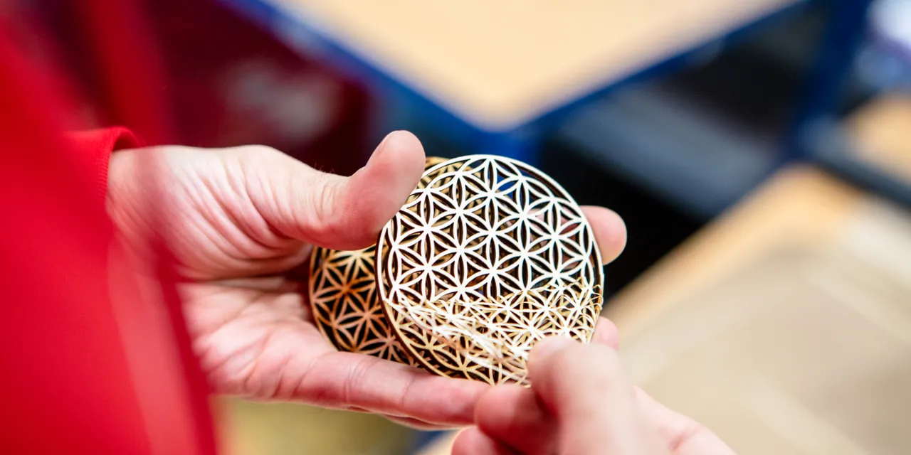 Person holding intricately cut wooden coasters made with Trotec CO₂ laser cutter