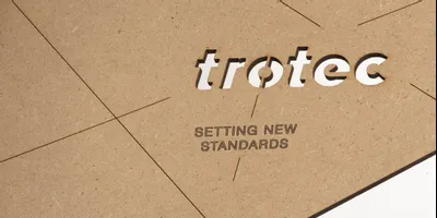 Trotec Laser geschnittene und gravierte MDF-Platte mit Logo und dem Slogan 'Setting New Standards'.