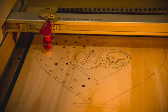 Trotec laser cutter engraving heart-shaped wood design with Love text using CO₂ laser
