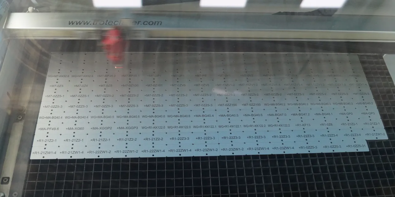 La machine de découpe laser Trotec grave des numéros de série sur une feuille de métal à l'intérieur du banc de la machine.