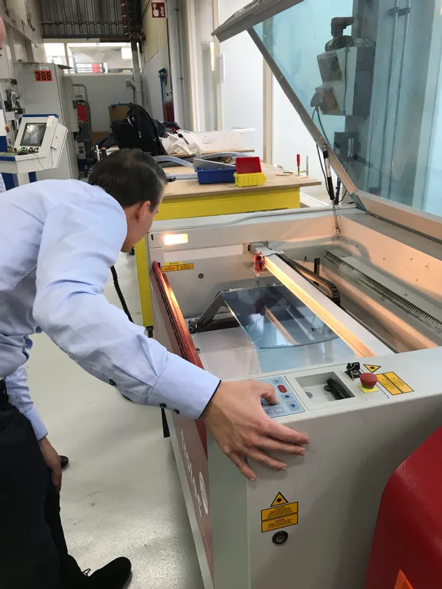 Operator inspecting Trotec Speedy series CO₂ laser engraver during material processing