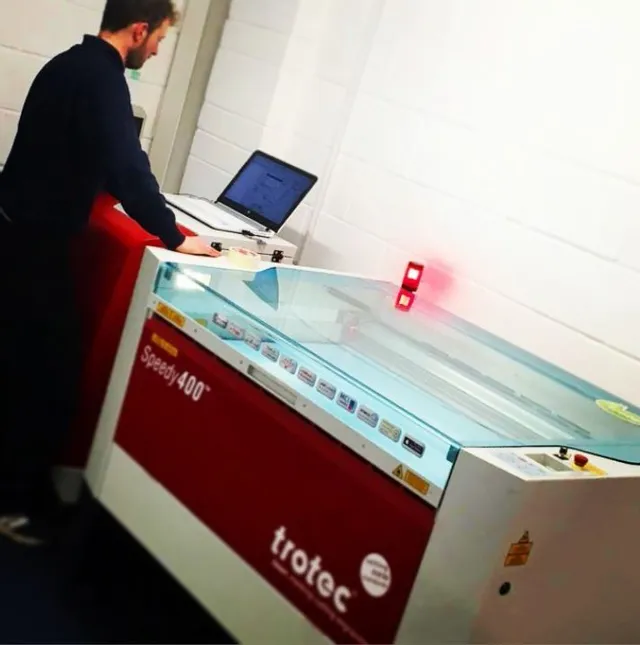 Operator using Trotec Speedy 400 CO₂ laser engraver with connected laptop